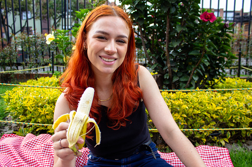 beautiful young woman eating banana in a park