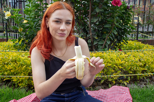 beautiful young woman eating banana in a park