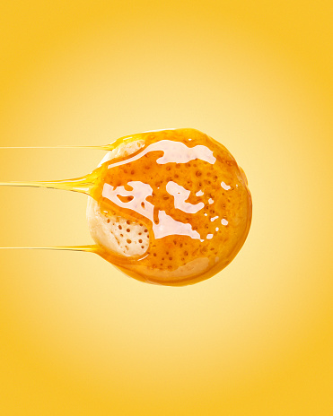 Honey is seen dripping sideways off an english muffin or crumpet.
