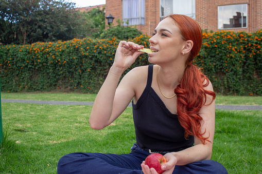 beautiful young woman eating pieces of mango in a park