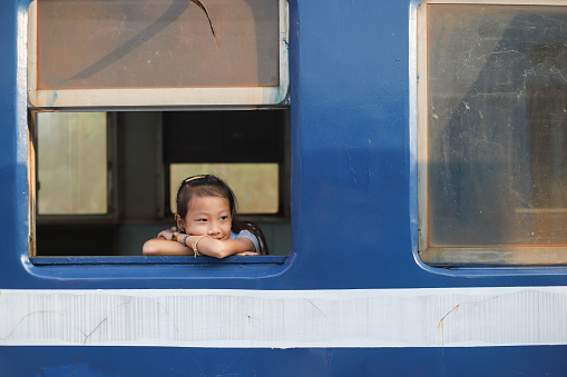 An Asian girl sits on the train and leans against the window to look at the scenery outside the window.  The picture shows the concept of leisure and travel.