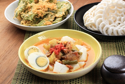 Lontong Sayur Padang, Vegetable Curry with Rice Pressed Cake, Served with Boiled Egg. Served on Wooden Table with Yellow Plate. Served with Krupuk Warung on Background