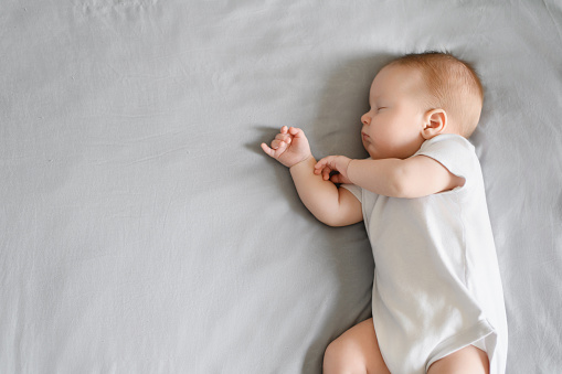 Cute baby sleeps peacefully in his crib at home, lying on his side. The concept of independent sleep, childhood protection.Copy space. Independent sleep. Children Day.