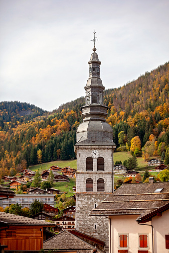 A ski resort town in the French Alps during the off-season, with a grand clock tower rising above the tranquil, leaf-strewn village landscape. Peaceful calm retreat in downtime. Travel concept