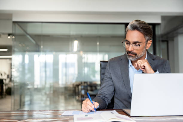 istock Middle-age Hispanic man using laptop computer for business studying, watch online virtual webinar training meeting, video call. Focused mature Indian or Latin businessman work in office, copy space. 1936243201