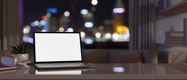 istock Modern apartment living room at night with a white-screen laptop computer and accessories on a table 1936262677
