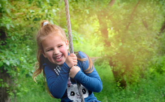 Child girl  having  fun outdoors swinging on wooden homemade swing tied to a tree with a rope