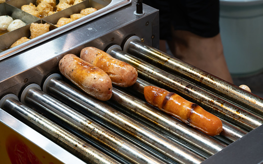 Hot dog with grilled sausage, tomato and lettuce on dark background. American hotdog