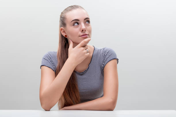 Young woman with hand on chin looks up, contemplating, her striped shirt suggesting casual thoughtfulness