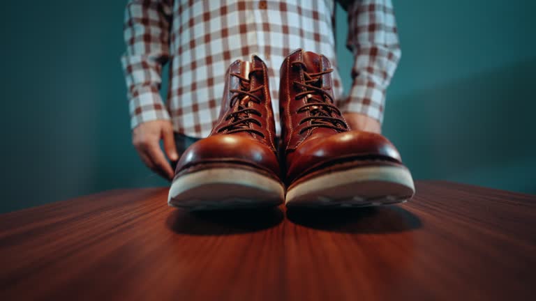 Unrecognizable man leaving pair of shiny brown leather shoes on the table