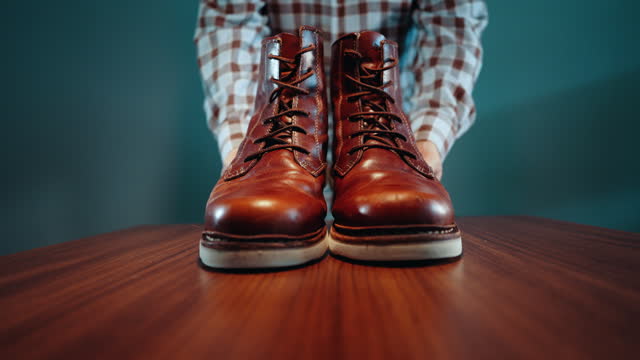 Unrecognizable man leaving pair of shiny brown leather shoes on the table