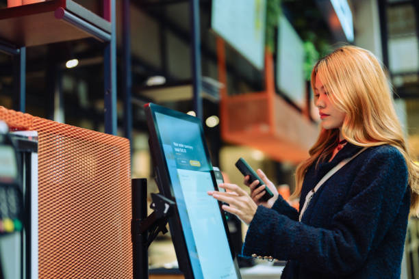 E-money transfer, contactless payment concept. Women in casual clothing paying using automatic payment machine and smartphone. contactless airport stock pictures, royalty-free photos & images