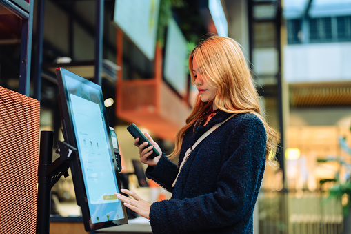 Women in casual clothing paying using automatic payment machine and scanning through smartphone.
