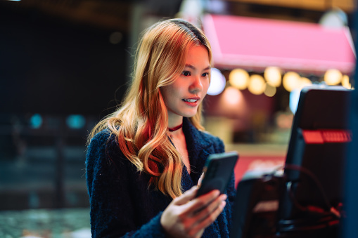 Women in casual clothing paying using automatic payment machine and scanning through smartphone.