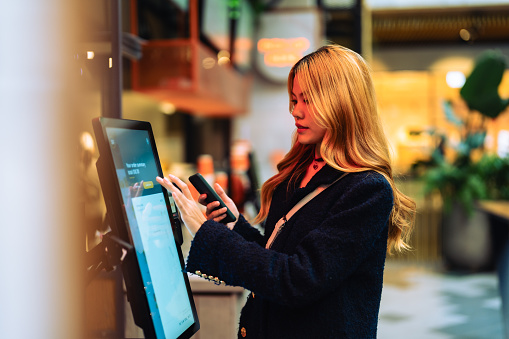 Women in casual clothing paying using automatic payment machine and smartphone.