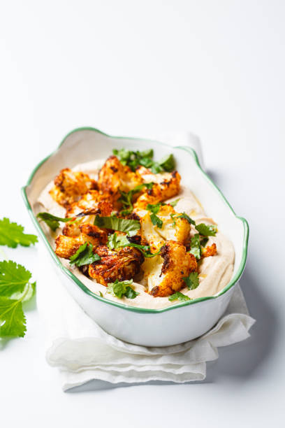 istock Baked spicy cauliflower with hummus and cilantro, white background. 1936545129
