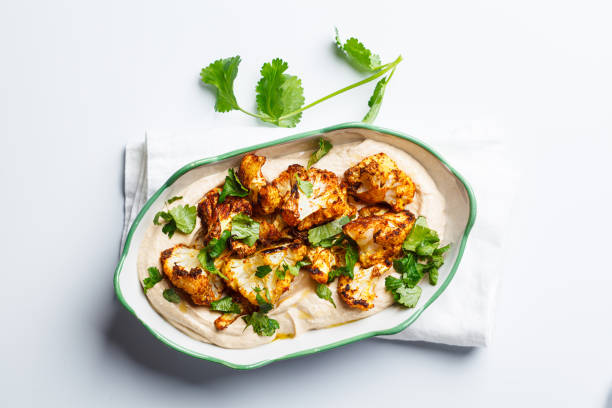 Baked spicy cauliflower with hummus and cilantro, white background.