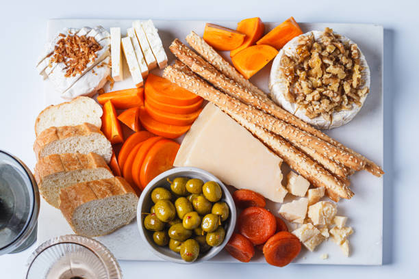 istock Cheese platter with persimmons, olives and wine on white marble board for party. 1936546667