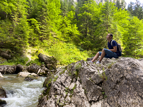 A young man sits on a rock by a mountain river