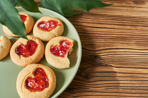 Biscuits with strawberry jam on plate on wooden table, closeup