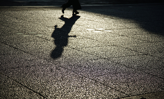 Silhouette reflected on the cobblestones of a person walking on the street in the evening