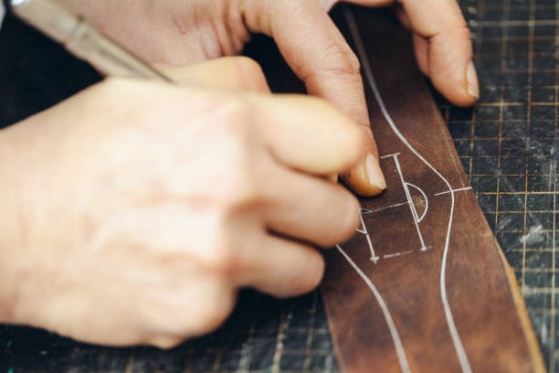 istock Close up of a shoemaker or artisan worker hands. Leather craft tools on old wood table. 1936665639