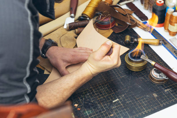 istock Close up of a shoemaker or artisan worker hands. Leather craft tools on old wood table. 1936667133