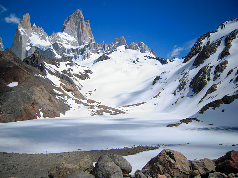 Distant hiker admiring the majestic Fitz Roy covered with snow from Lagoon de Los Tres, Patagonia