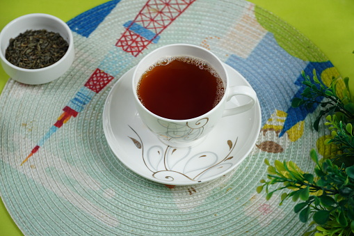 Looking down on a glass of tea and dried tea leaves on white painted wooden table