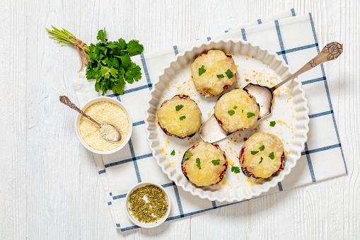 low-carb and gluten free mini eggplant pizzas with marinara sauce, mozzarella, monterey jack and parmesan cheese in baking dish on white wooden table with fresh coriander, flat lay, free space