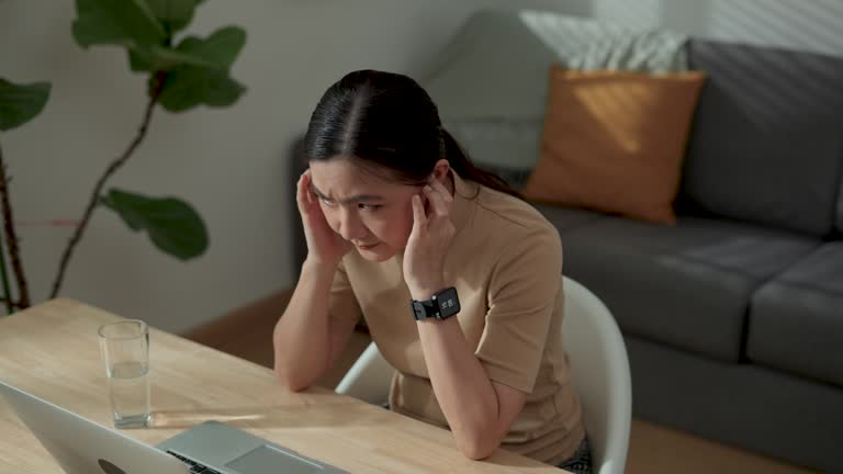 Asian woman using laptop for working at home office feel bored and annoyed covering her ears by hands.