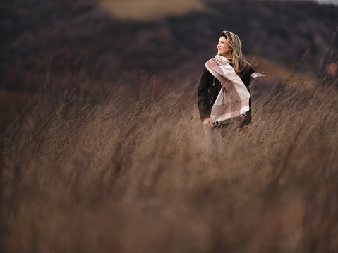 Carefree woman walking through tall grass in autumn day on a hill. Photographed in medium format. Copy space.