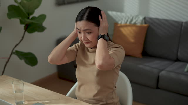 Asian woman using laptop for working at home office feel bored and annoyed covering her ears by hands.