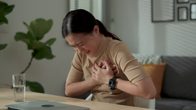 Asian woman suffering from chest pain sitting at home office.
