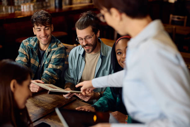istock Happy friends choosing order from a menu with help of a waitress in a pub. 1936791438
