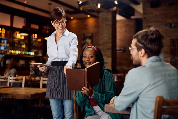 istock Happy waitress recommending an order from a menu to her customers in a pub. 1936791951