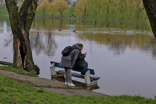 Kyiv, Ukraine - April 16, 2021: A girl sits on a flooded bench on the city embankment. The high water of the Dnipro River after the rains and the melting of a large amount of snow. Natural disaster.