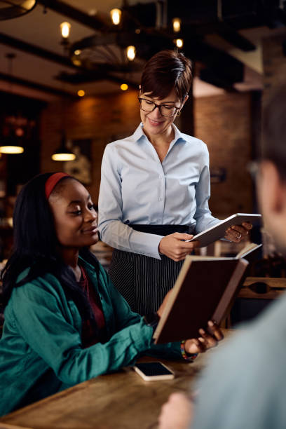 istock Happy waitress using digital tablet while taking order from black woman in a bar. 1936796696