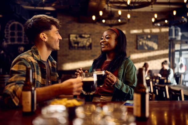 istock Happy black woman and her boyfriend talking while drinking beer in a bar. 1936801049