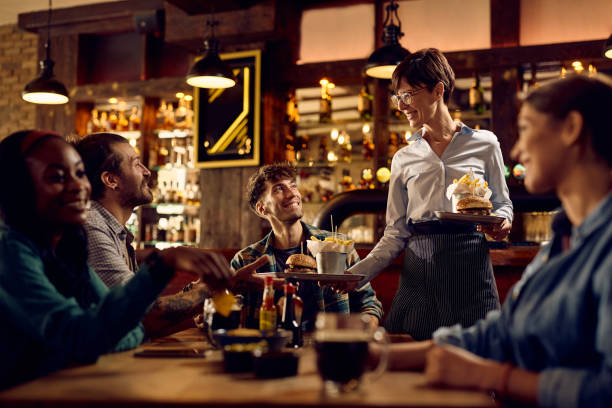 camarera feliz sirviendo comida a un grupo de amigos en un pub. - restaurante fotografías e imágenes de stock