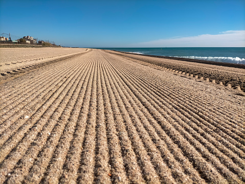 Playa de Vilassar de Mar-Barcelona, a primera hora de la mañana en verano, recién cepillada con el tractor.
Se observan líneas horizontales que desaparecen a lo largo de la playa, el cielo azul y el mar Mediterráneo a mano derecha. photo