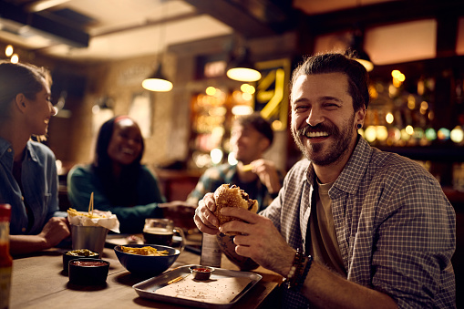 Cheerful man enjoying in food and drinks with his friends in a pub and looking at camera.