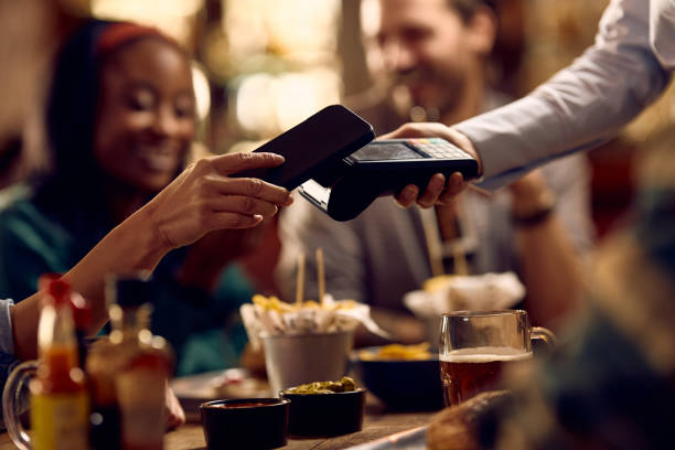istock Close up of man using smart phone while paying contactless in a pub. 1936805865