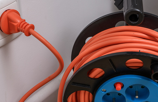 Power consumption, reel extension cord plugged into an electrical outlet isolated closeup