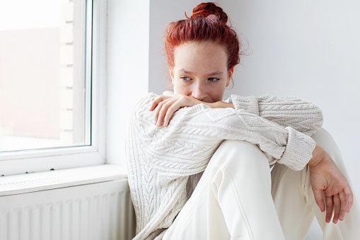 Depressed Sad young Woman sitting on floor near radiator. Difficulty, failure and exhaustion. Thoughtful Worried Teenage Girl suffering depression feeling alone at home. Mental health concept