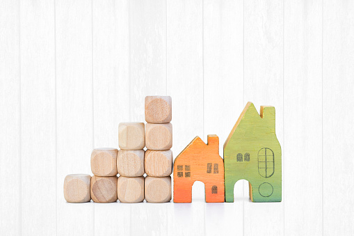 Miniature house model with wooden cube stack on white wood background, building block to success