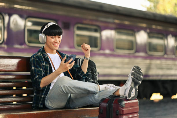 istock Young man sitting on bench and using mobile phone, waiting for the train on the platform. 1936869840