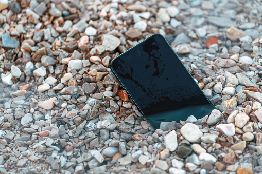 Lost smart phone device in pebbles on seaside beach in summer morning, selective focus