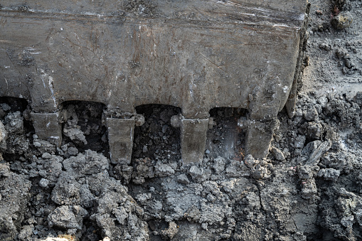 Closeup dirty bucket of backhoe working at construction site. Bucket teeth of backhoe digging soil. Crawler excavator digging on soil. Excavating machine. Earthmoving machine. Excavation vehicle.