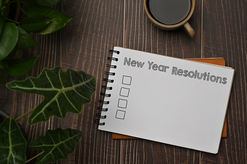 New Year Resolutions text on a spiral notebook with cup of coffee and glasses on wooden table.